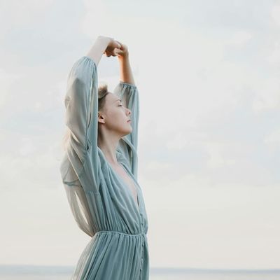 Person taking a deep breath outdoors with eyes closed.